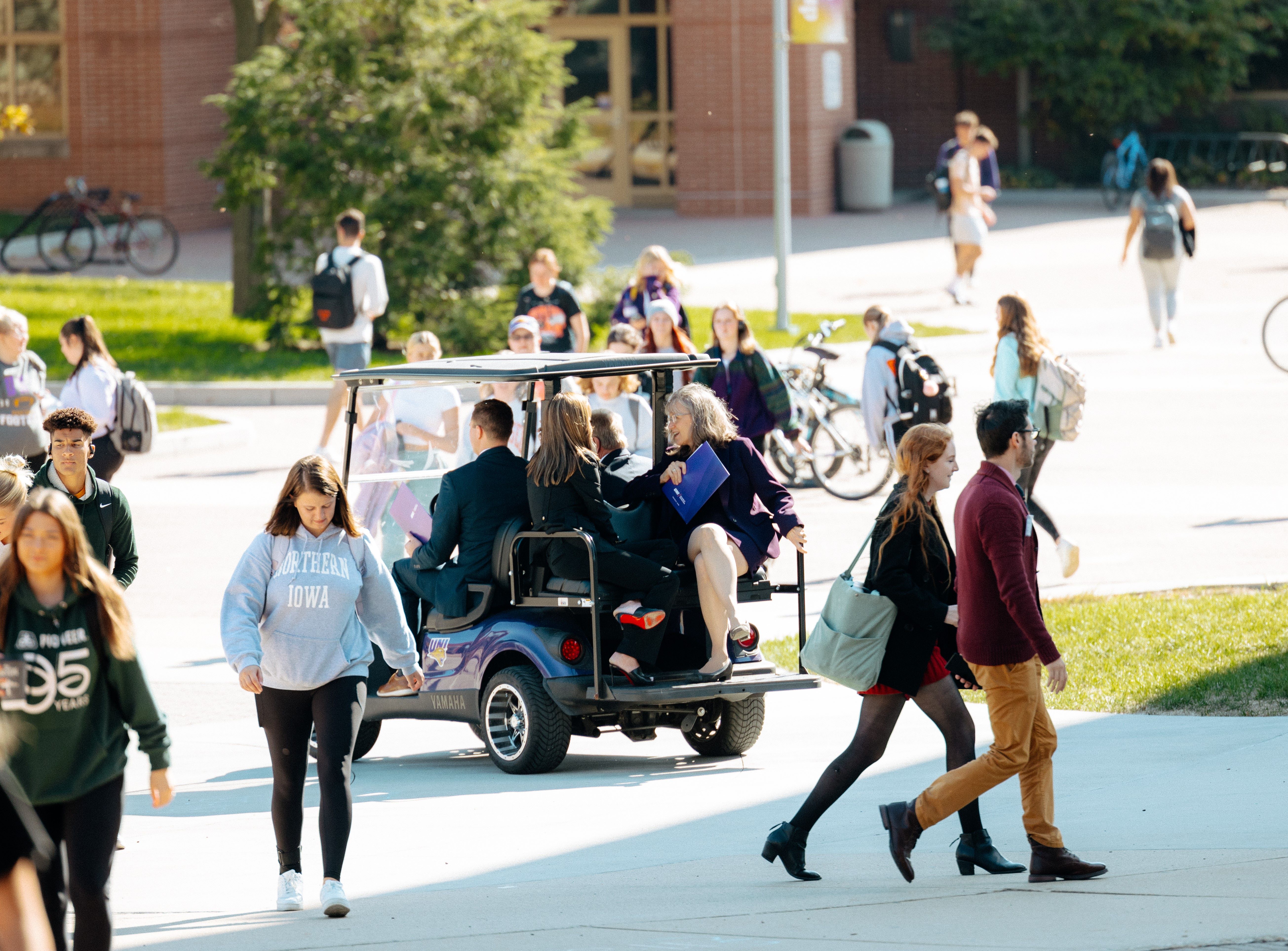 people riding in a golf cart in the middle of a busy campus 